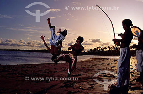  Homens jogando capoeira ao entardecer ao som de pandeiro e berimbaus e coqueiros ao fundo - BA - Brasil - Data: 2003 