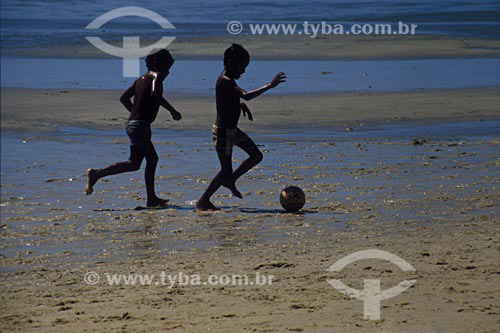 Imagem de crianças jogando bola na beira da praia.