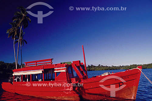  Barco de pescador vermelho com coqueiros e céu azul no mar da Ilha de Itaparica  - BA - Brasil

 A Ilha de Itaparica situa-se na Baía de Todos os Santos e seu conjunto arquitetônico, paisagístico e urbanístico é Patrimônio Histórico Nacional desde 28-04-1980.  - Salvador - Bahia - Brasil