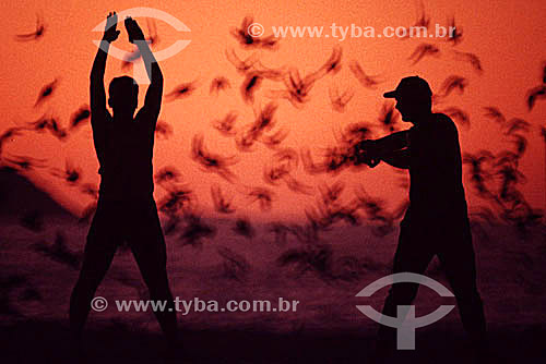  Silhueta de dois homens fazendo exercícios físicos ao alvorecer na Praia de Copacabana com revoada de pássaros ao fundo - Rio de Janeiro - RJ - Brasil  - Rio de Janeiro - Rio de Janeiro - Brasil