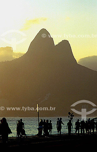  Silhueta de pessoas caminhando no calçadão da Praia de Ipanema ao pôr-do-sol com o Morro Dois Irmãos   ao fundo - Rio de Janeiro - RJ - Brasil

  Patrimônio Histórico Nacional desde 08-08-1973.  - Rio de Janeiro - Rio de Janeiro - Brasil