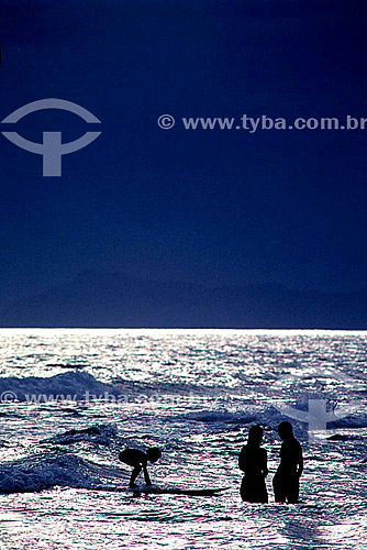  Silhueta de casal e criança surfando nas águas da Praia da Barra da Tijuca, prateadas pelo reflexo do sol - Rio de Janeiro - RJ - Brasil  - Rio de Janeiro - Rio de Janeiro - Brasil