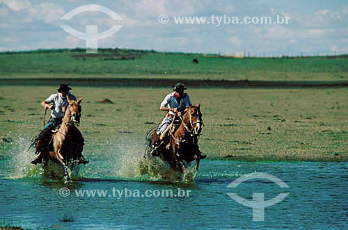  Dois homens gaúchos atravessando rio à cavalo - RS - Brasil  - Rio Grande do Sul - Brasil