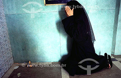  Mulher vestida de preto ajoelhada rezando 