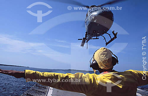  Helicóptero pousando no Navio Hospitalar Oswaldo Cruz e controlador de vôo com protetor para o ouvido em primeiro plano - Amazônia - Brasil  