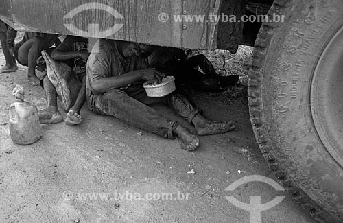  Assunto: Cortadores de cana almoçando debaixo de um ônibus para se proteger da chuva / Local: Bahia (BA) - Brasil / Data: 04/2007 