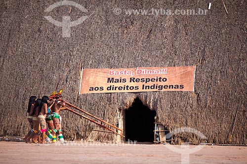  Índios Yawalapiti tocando a flauta Uruá no ritual do Kuarup com uma faixa de protesto em que se lê: 
