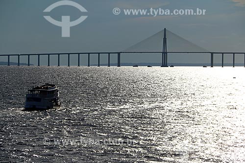  Silhueta de chalana - embarcação regional - no Rio Negro com a Ponte Rio Negro ao fundo durante o pôr do sol  - Manaus - Amazonas (AM) - Brasil
