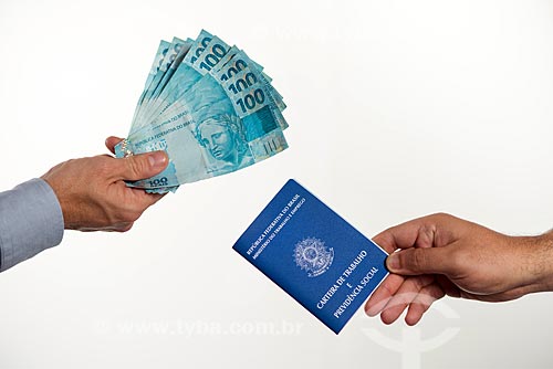  Detalhe de mão segurando notas de 100 reais - à esquerda - e mão segurando carteira de trabalho - à direita  - Rio de Janeiro - Rio de Janeiro (RJ) - Brasil