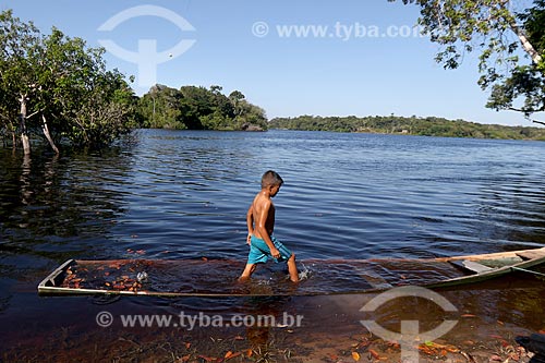  Menino ribeirinho da comunidade ribeirinha tumbira brincando em canoa quase encoberta no Rio Negro - Parque Nacional de Anavilhanas  - Novo Airão - Amazonas (AM) - Brasil