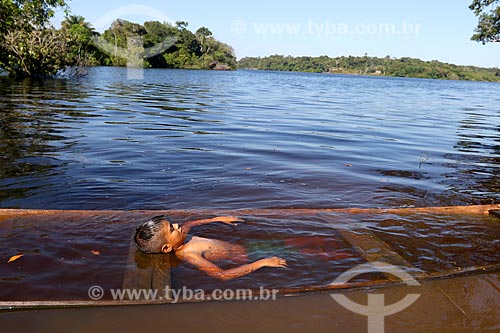  Menino ribeirinho da comunidade ribeirinha tumbira brincando em canoa quase encoberta no Rio Negro - Parque Nacional de Anavilhanas  - Novo Airão - Amazonas (AM) - Brasil