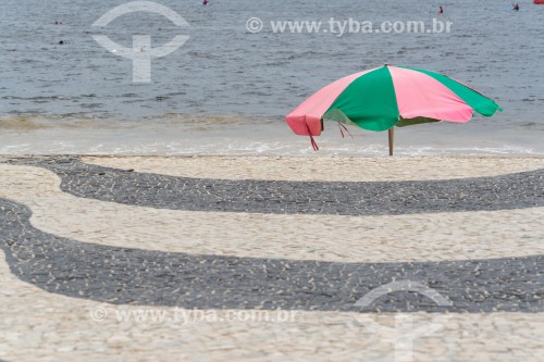 Pedras portuguesas com desenho tradicional de ondas no calçadão de Copacabana com Guarda sol verde e rosa (Referência a Escola de Samba Mangueira) ao fundo - Rio de Janeiro - Rio de Janeiro (RJ) - Brasil