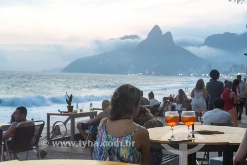 Pessoas em mesas de bar ao entardecer na praia do Arpoador com o Morro Dois Irmãos ao fundo - Rio de Janeiro - Rio de Janeiro (RJ) - Brasil