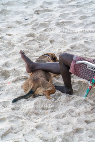 Homem apoiando a perna sobre cachorro na areia da Praia do Arpoador - Rio de Janeiro - Rio de Janeiro (RJ) - Brasil
