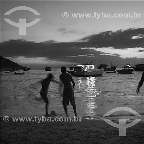  Silhouette of boys playing football at the beach with boats on the sea in the background - Guaratiba Beach, at the south coast of the state of Rio de Janeiro, near the Restinga da Marambaia (Marambaia Coastal Plain) - Rio de Janeiro city - Brazil 