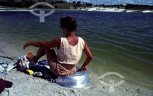  Woman seating on a basin of aluminum washing clothes with the help of the feet on Lagoa de Abaeté (Abaete Lagoon) - Salvador city - Bahia state - Brazil 