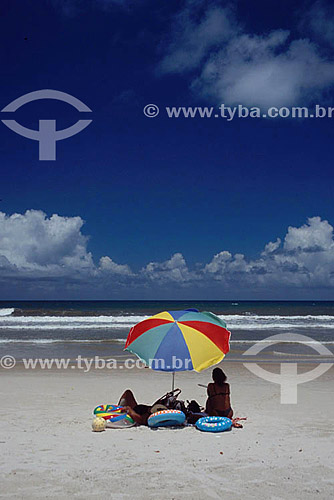  Woman seating under a colored beach umbrella beside child`s buoys - 