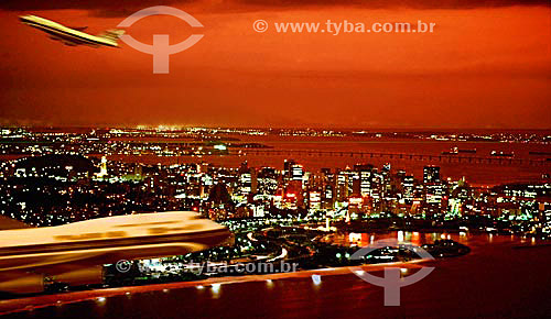  Aerial view of the Aterro do Flamengo* at twilight  with the illuminated buildings from the center of Rio de Janeiro city with commercial airplanes passing in the foreground and the Rio-Niteroi Bridge in the background - Rio de Janeiro state - Brazi 