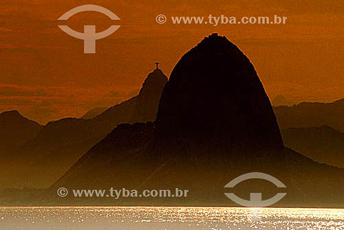  Silhouette of Sugar Loaf Mountain* in the foreground with Cristo Redentor (Christ the Redeemer) in the background at dawn - Rio de Janeiro city - Rio de Janeiro state - Brazil  *Commonly called Sugar Loaf Mountain, the entire rock formation also inc 