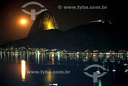  Silhouette of Sugar Loaf Mountain* at night with the moon to its left, the lights of the Urca district below and boats in the foreground - Rio de Janeiro city - Rio de Janeiro state - Brazil  *Commonly called Sugar Loaf Mountain, the entire rock for 