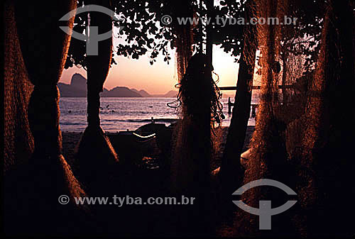  Copacabana Beach at daybreak, with the silhouette of fishing nets hanging from trees and a boat resting on the beach in the foreground, and Sugar Loaf Mountain in the background. - Rio de Janeiro city - Rio de Janeiro state - Brazil 