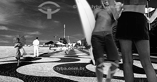  Surfer and woman meet at the Copacabana sidewalk in the foreground with people passing in second plan - Leme Beach - Rio de Janeiro city - Rio de Janeiro state - Brazil 