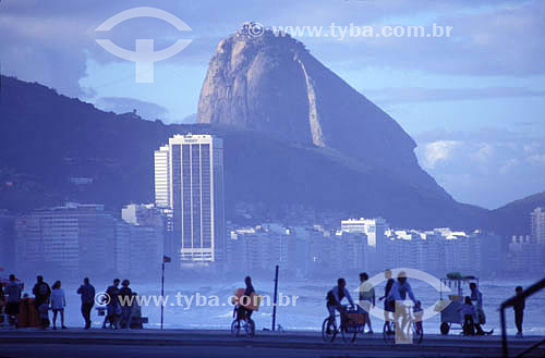  Silhouette of people on Copacabana Promenade and bicycle path with part of Sugar Loaf Mountain* above the buildings in the background - Rio de Janeiro city - Rio de Janeiro state - Brazil  * Commonly called Sugar Loaf Mountain, the entire rock forma 