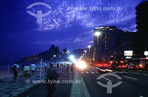  Night falls on Ipanema Beach as some people walk on the Promenade, others jog and bicycle on the bicycle path, with the lights of cars moving along Av. Vieira Souto (Vieira Souto Avenue) and the Morro Dois Irmaos* (Two Brothers Mountain) in the back 