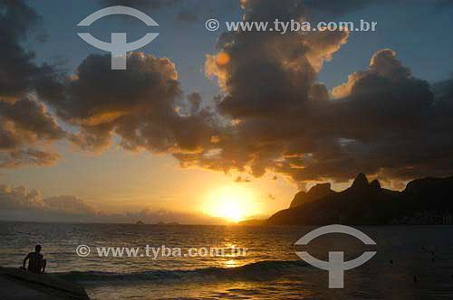  Man lying down at Ipanema Beach at sunset with the Morro Dois Irmaos (Two Brothers Mountain)* in the background - Rio de Janeiro city - Rio de Janeiro state - Brazil  *The two Brothers Mountain is National Historic Site since 08-08-1973 