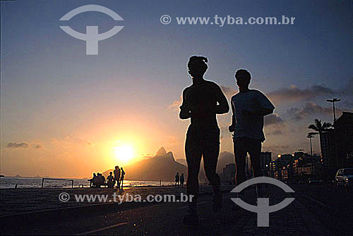  Silhouette of a couple jogging on the bicycle path on Ipanema Beach at sunset with the Morro Dois Irmaos (Two Brothers Mountain) in the background - Rio de Janeiro city - Rio de Janeiro state - Brazil 