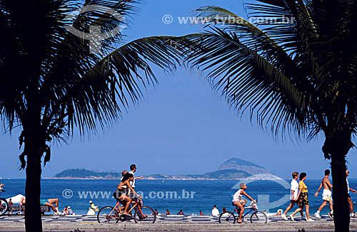  People walking at Ipanema sidewalk with palm trees in the foreground and the sea in the background - Rio de Janeiro city - Rio de Janeiro state - Brazil 