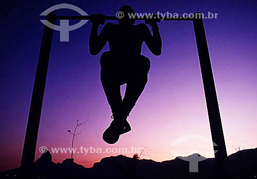  Silhouette of a man doing chin-ups on Ipanema neighborhood at sunset with Rock of Gavea and Morro Dois Irmaos (Two Brothers Mountain) in the background to the left - Rio de Janeiro city - Rio de Janeiro state - Brazil 