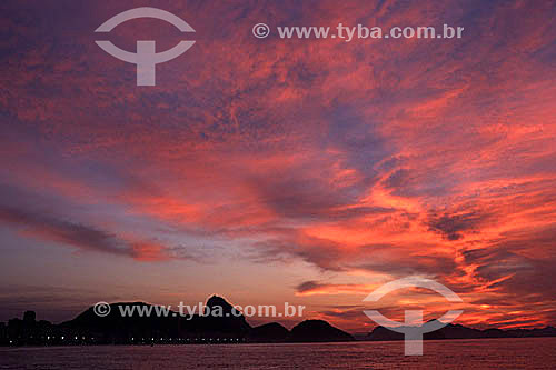  Silhouette of Sugar Loaf Mountain against the reddish-brown reflection of the sunset on the clouds, with Guanabara Bay in the foreground - Rio de Janeiro city - Rio de Janeiro state - Brazil 