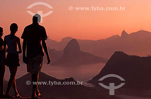  Young adults admiring the view of the mountains of Rio de Janeiro at sunset, with Sugar Loaf Mountain* in the center and Cristo Redentor (Christ the Redeemer) behind to the left - Rio de Janeiro city - Rio de Janeiro state - Brazil  * Commonly calle 