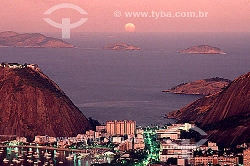  Lights of buildings in the neighborhood of Urca at sunset, with Praia Vermelha (Red Beach) in the center, part of Sugar Loaf Mountain (1) to the left, part of Morro da Babilonia (Babylonia Mountain) (2) to the right, and the rising moon on the horiz 