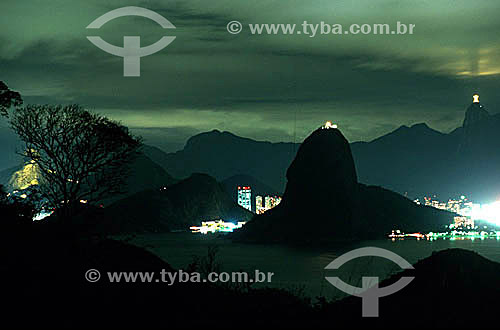  Night time silhouette of Sugar Loaf Mountain* as seen from the city from Niteroi, surrounded by lights from buildings in the neighborhoods of Urca and Botafogo, with Cristo Redentor (Christ the Redeemer) in the upper right, and part of Morro Dois Ir 