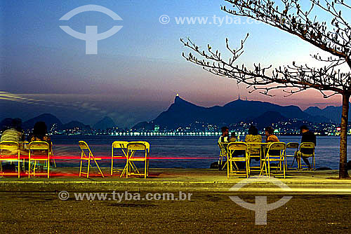  Lights of cars passing, and people enjoying the sunset and beer on Praia Boa Viagem (Boa Viagem Beach) in the city of Niteroi, with the illuminated buildings of Flamengo Beach and Christ the Redeemer in the background - Niteroi city - Rio de Janeiro 