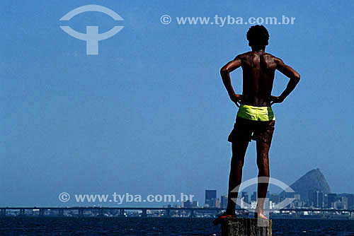  Young man looking across Guanabara Bay, with Ponte Rio-Niteroi (Rio-Niteroi Bridge) and Sugar Loaf Mountain in the background - Ilha do Governador (Governor´s Island) - Rio de Janeiro city - Rio de Janeiro state - Brazil 