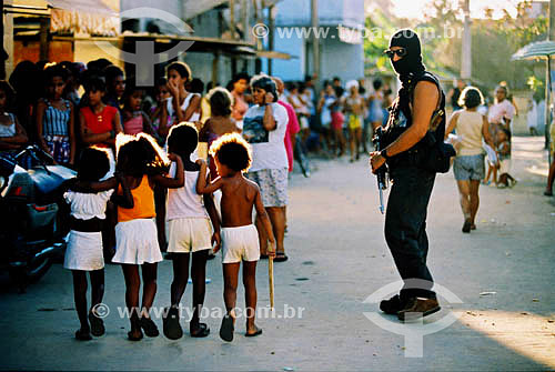  Policeman with hidden face and weapon beside children in the favela of Vigario Geral - Rio de Janeiro city - Rio de Janeiro state - Brazil 