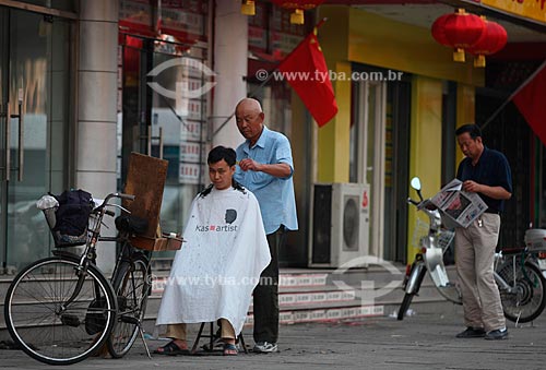  Subject: In Guomao district, a barber who uses his bike as saloon, cuts the hair  of his client  / Place:  Beijing city - China  / Date: Agosto de 2008 