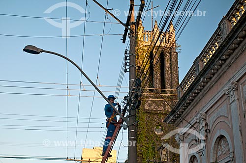 Labourer doing maintenance on the telephone network with the Anglican Cathedral of the Redeemer (1892) - also known as Cabeluda Church - in the background  - Pelotas city - Rio Grande do Sul state (RS) - Brazil