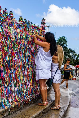  Women tying up colorful ribbons - grids of the Nosso Senhor do Bonfim Church (1754)  - Salvador city - Bahia state (BA) - Brazil