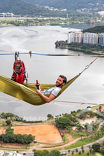  Man lying in a hammock on slackline strip with a bottle of wine - Cantagalo Hill with the Rodrigo de Freitas Lagoon in the background  - Rio de Janeiro city - Rio de Janeiro state (RJ) - Brazil