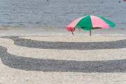 Portuguese stone with a traditional wave design on the Copacabana boardwalk with green and pink sun umbrella (Reference to Mangueira Samba School) in the background - Rio de Janeiro city - Rio de Janeiro state (RJ) - Brazil
