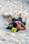 Young man lying on the sand with his head resting on a soccer ball - Rio de Janeiro city - Rio de Janeiro state (RJ) - Brazil