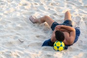 Young man lying on the sand with his head resting on a soccer ball - Rio de Janeiro city - Rio de Janeiro state (RJ) - Brazil
