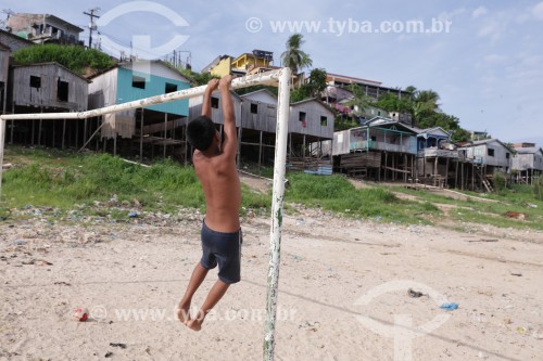 Criança brincando em trave de campo de várzea com casas de palafita ao fundo - Tefé - Amazonas (AM) - Brasil
