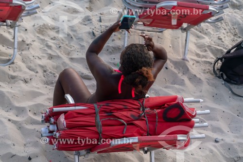 Mulher utilizando smartphone - Praia do Arpoador com cadeira de praia e guarda-sol para aluguel - Rio de Janeiro - Rio de Janeiro (RJ) - Brasil