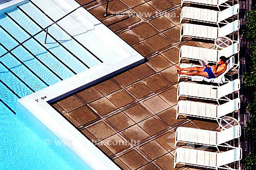  Leisure - Man reading in beach chair to the side of the swimming pool 