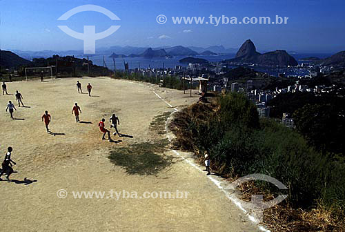  Soccer in a dirt field on the high of the Prazeres Hill, with the Guanabara Bay and the Sugar Loaf Mountain* in the background - Santa Tereza neighbourhood - Rio de Janeiro city - Rio de Janeiro state - Brazil  * Commonly called Sugar Loaf Mountain, 